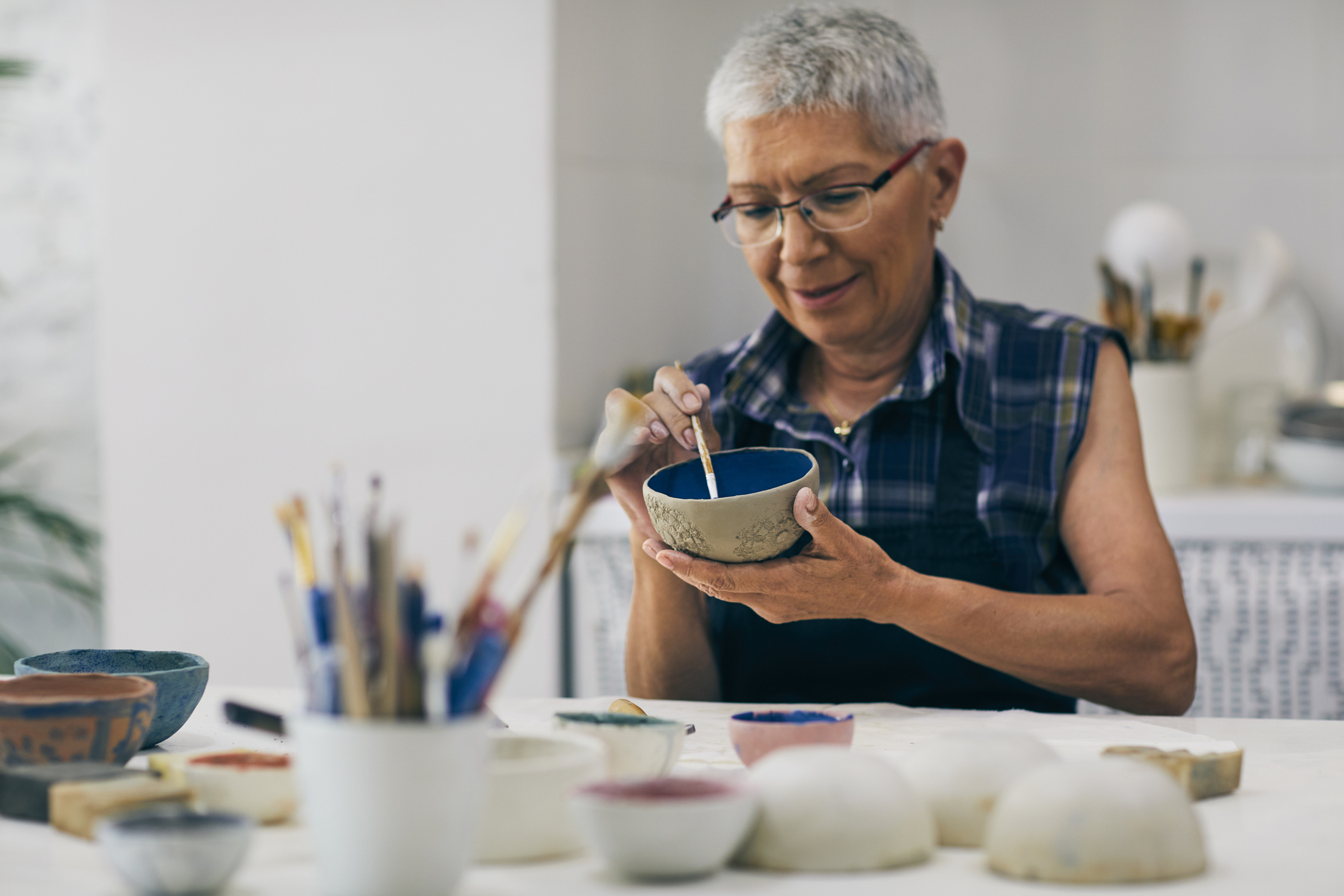 Senior woman decorating bowl made of clay on ceramics workshop.