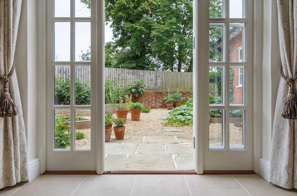 Curtains-with-tassel-tiebacks-hang-on-either-side-of-a-patio-door-that-leads-to-a-garden.