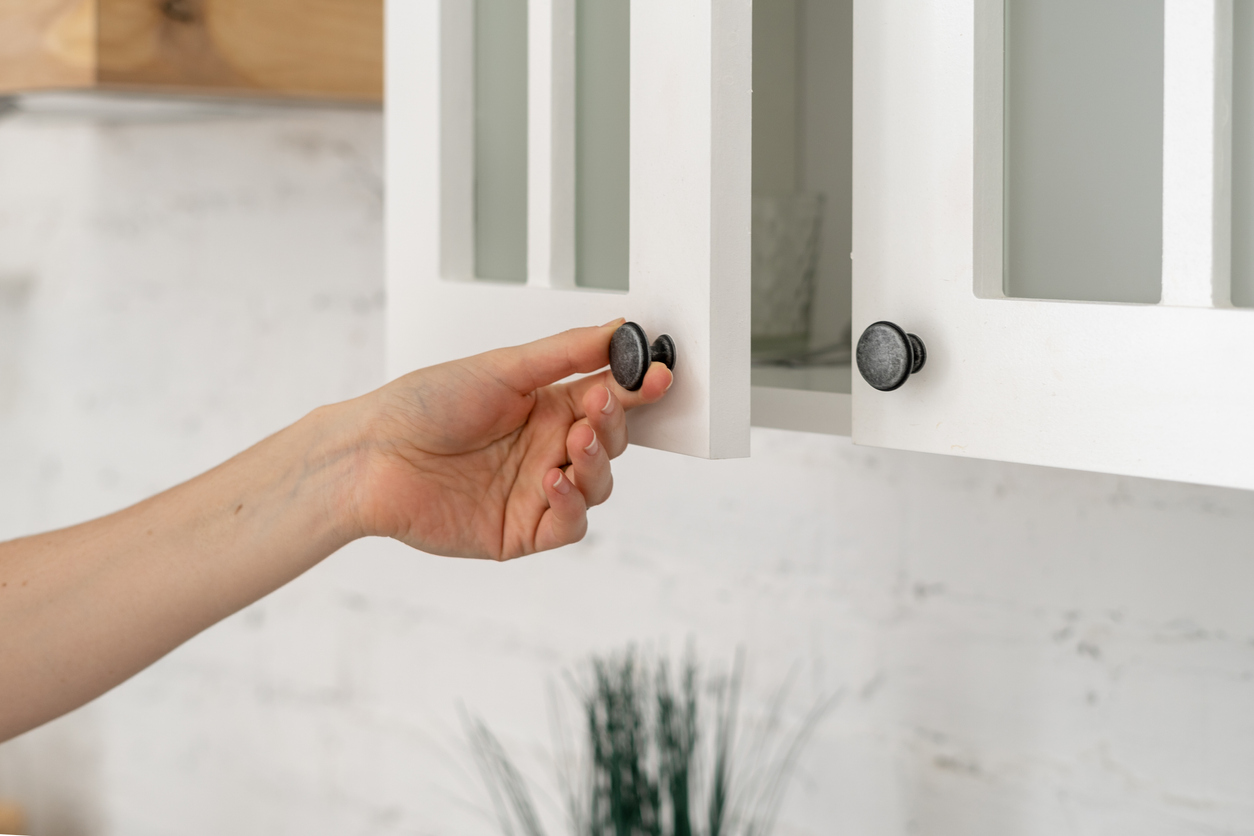 Cropped view of a woman's hand opening a white cabinet door, in house with modern interior