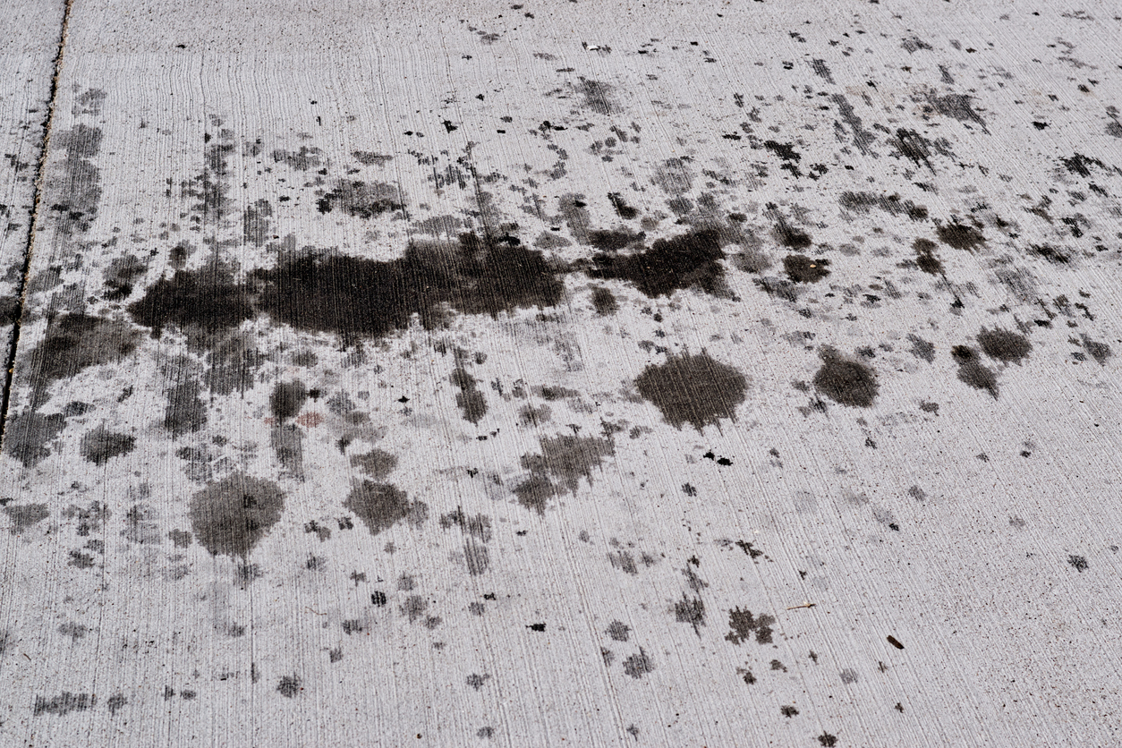 Vehicle motor oil stains on a concrete driveway with angled view. Concept image with copy space.