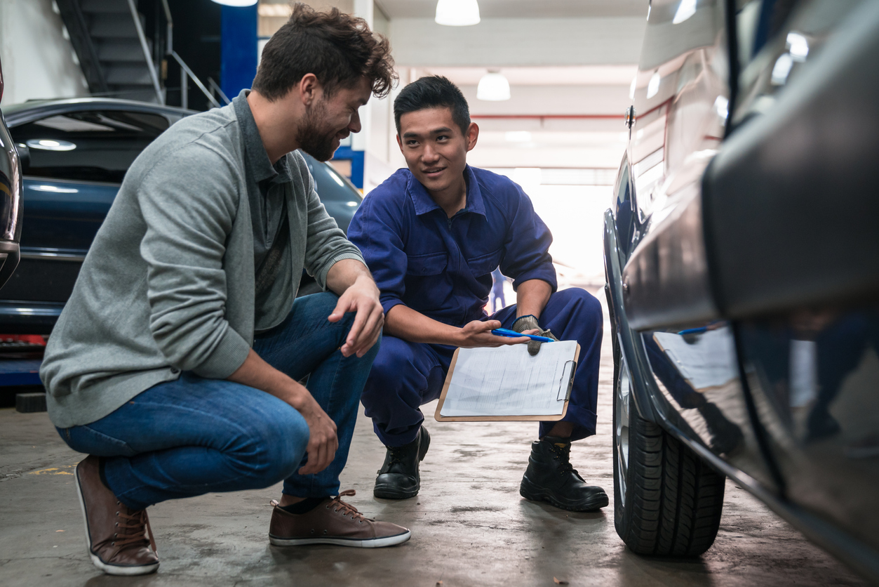 Car mechanic checking car wheel in the auto repair shop, talking with customer.