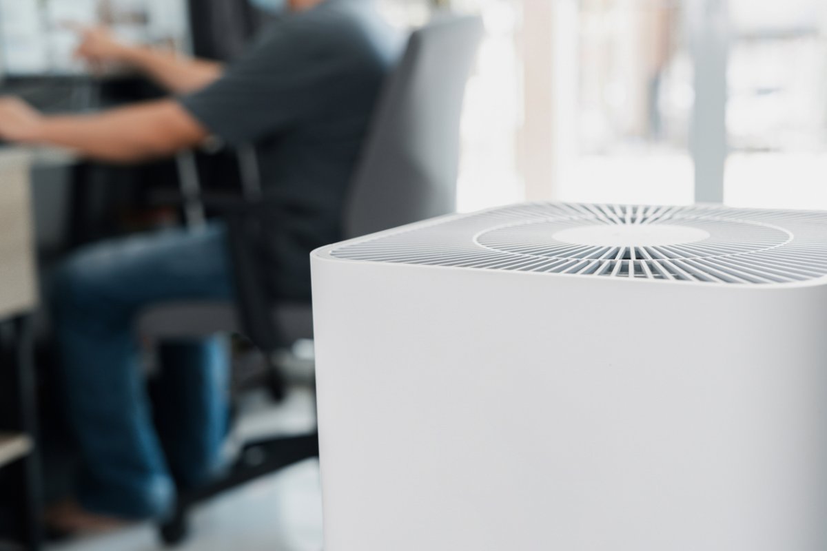 close view of Air purifier in the foreground with blurry view of man t his desk in the office