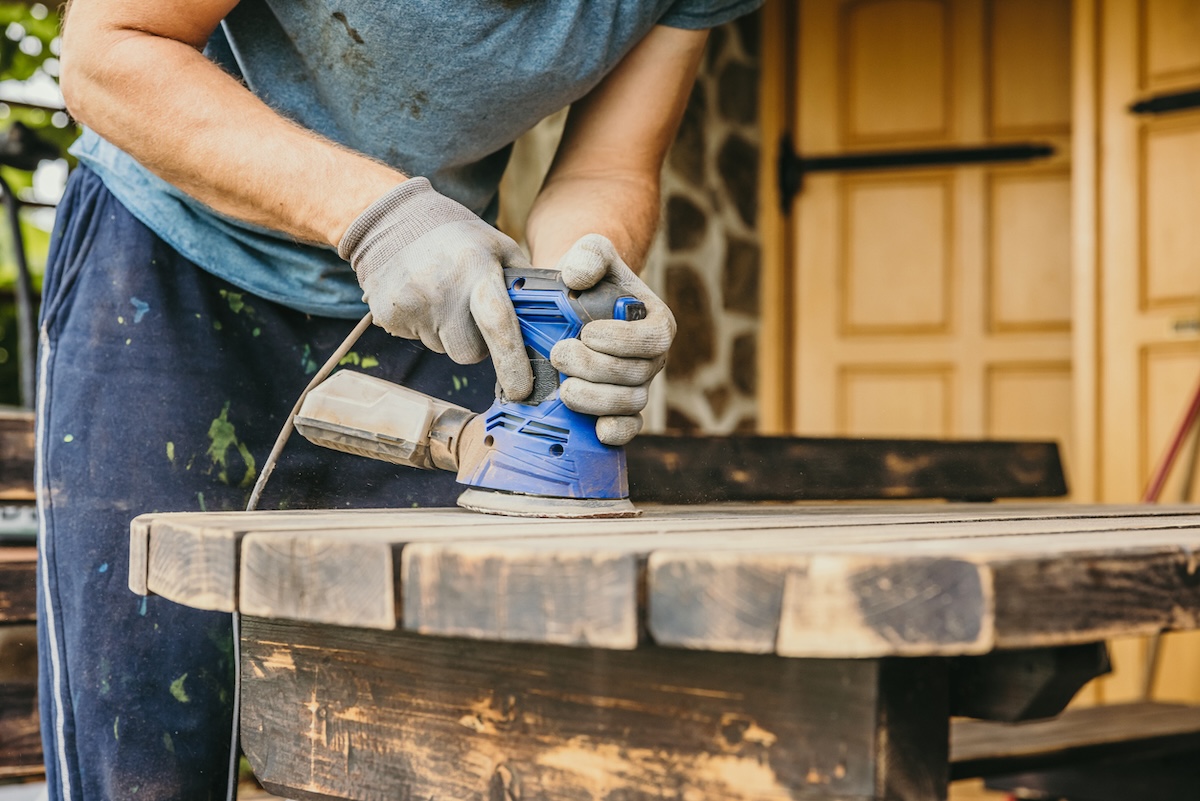 A person sanding off the old finish on an outdoor table to prepare for a new coat of paint.