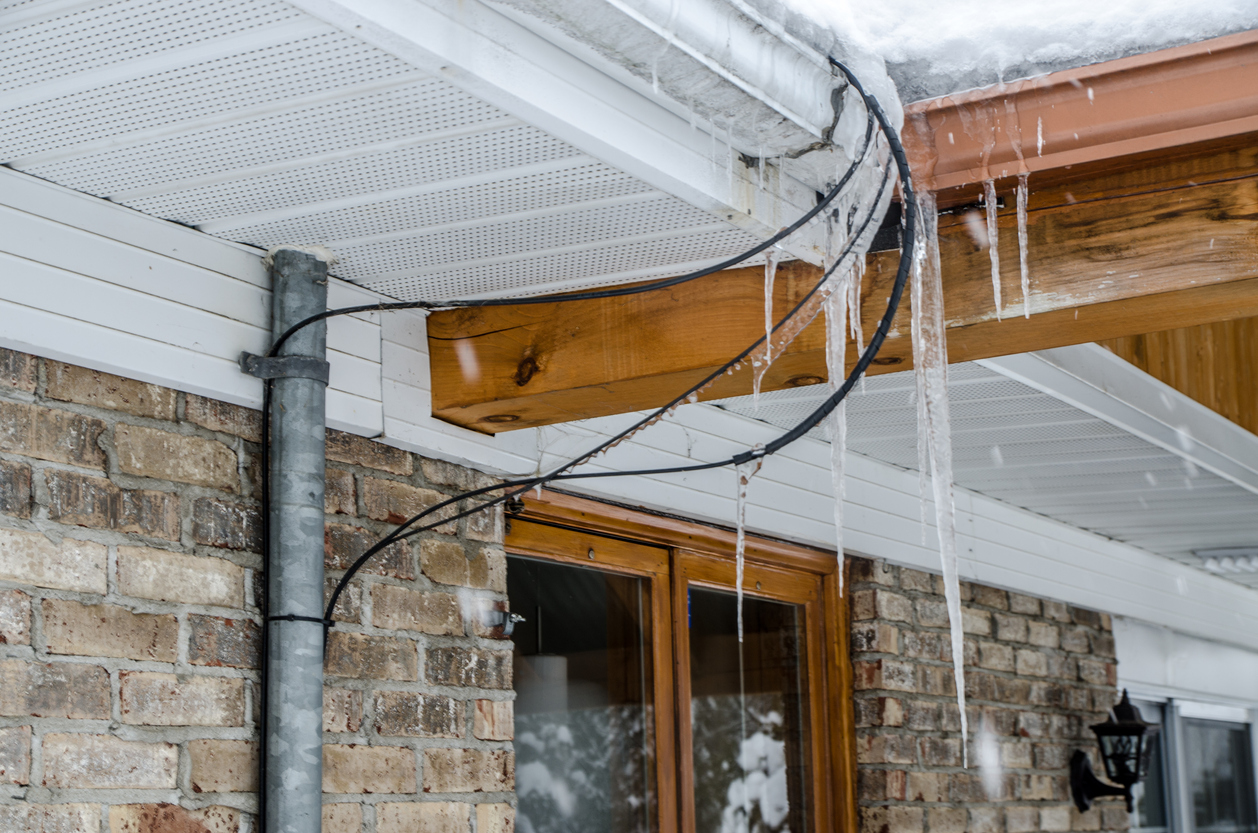 Gutter ice dams on roof of a house during warm day of winter