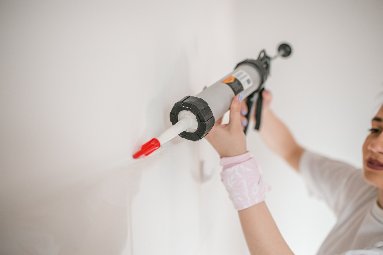 Cheerful millennial woman dressed in white T-shirt stand in an empty apartment, ready to paint the walls