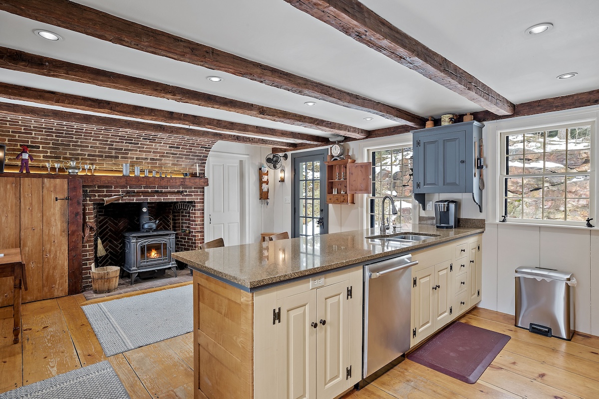 A modern keeping room inside a residential home just off of the kitchen with a wood burning stove inside a historical fireplace.