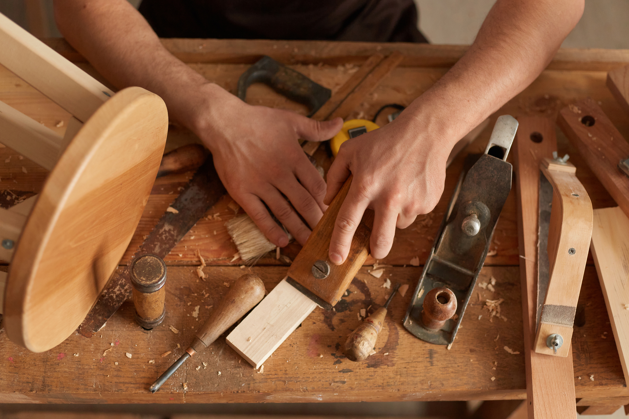 Closeup top view of carpenter man working and curving wood in his workshop, making wooden product in his joinery.