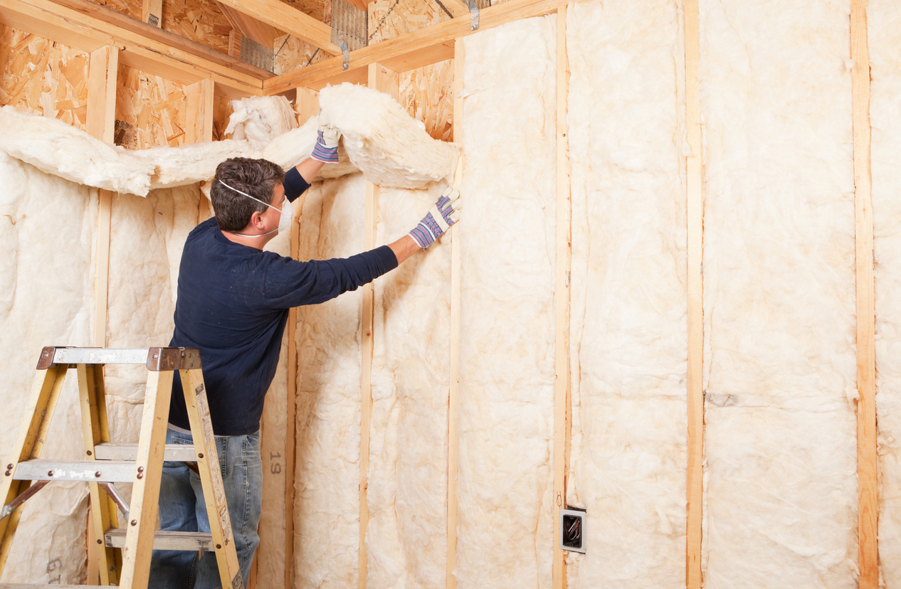 Man on ladder installs insulation in wall fram.