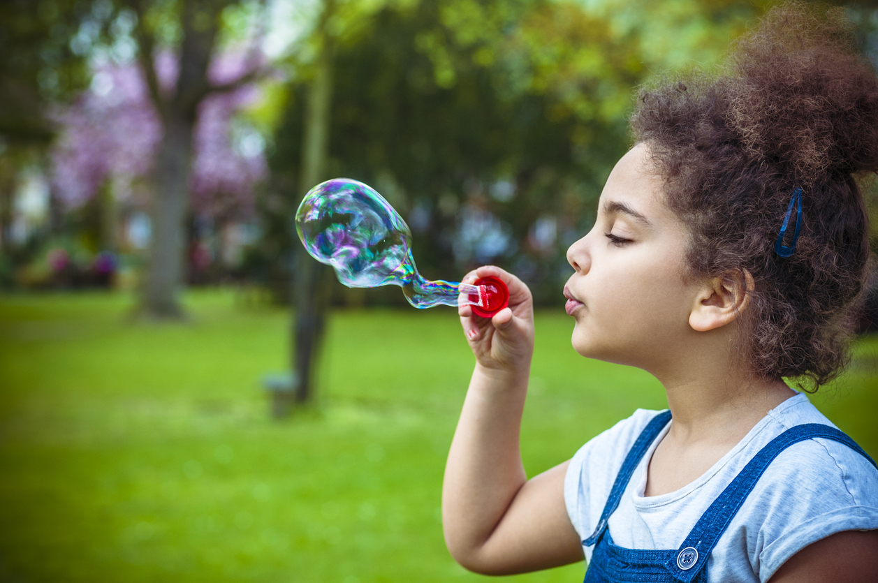 Child (7-8) Blowing Bubbles in Playground.