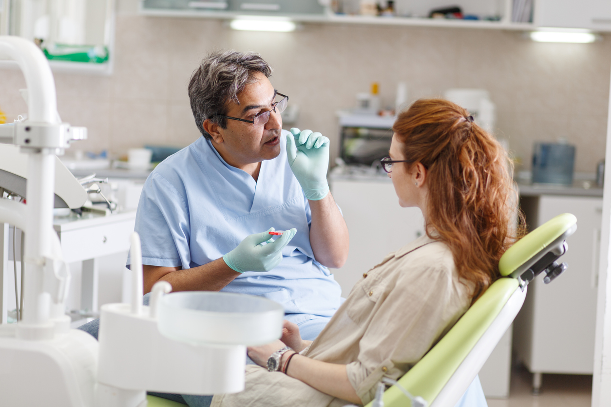 Senior male dentist in dental office talking with female patient and preparing for treatment.