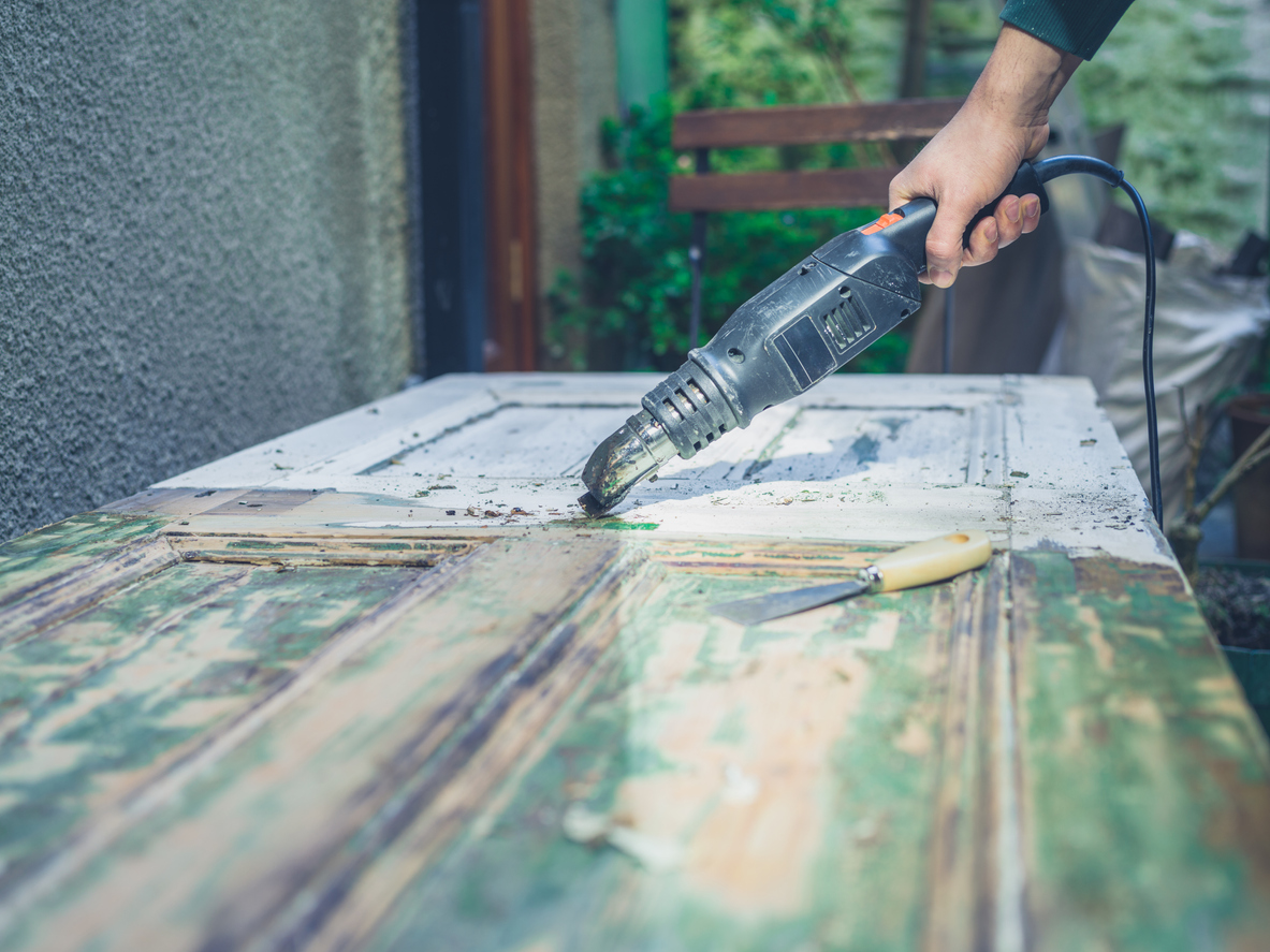 The hand of a young man stripping paint from a door with a heat gun