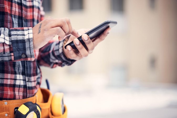 A handyman in flannel and a tool belt is on a smart phone.