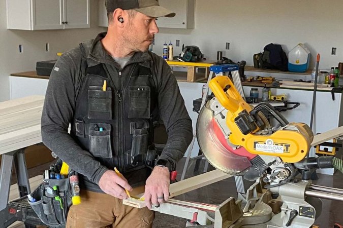 A person wearing a tool vest, hat, and earplugs while using a power saw.