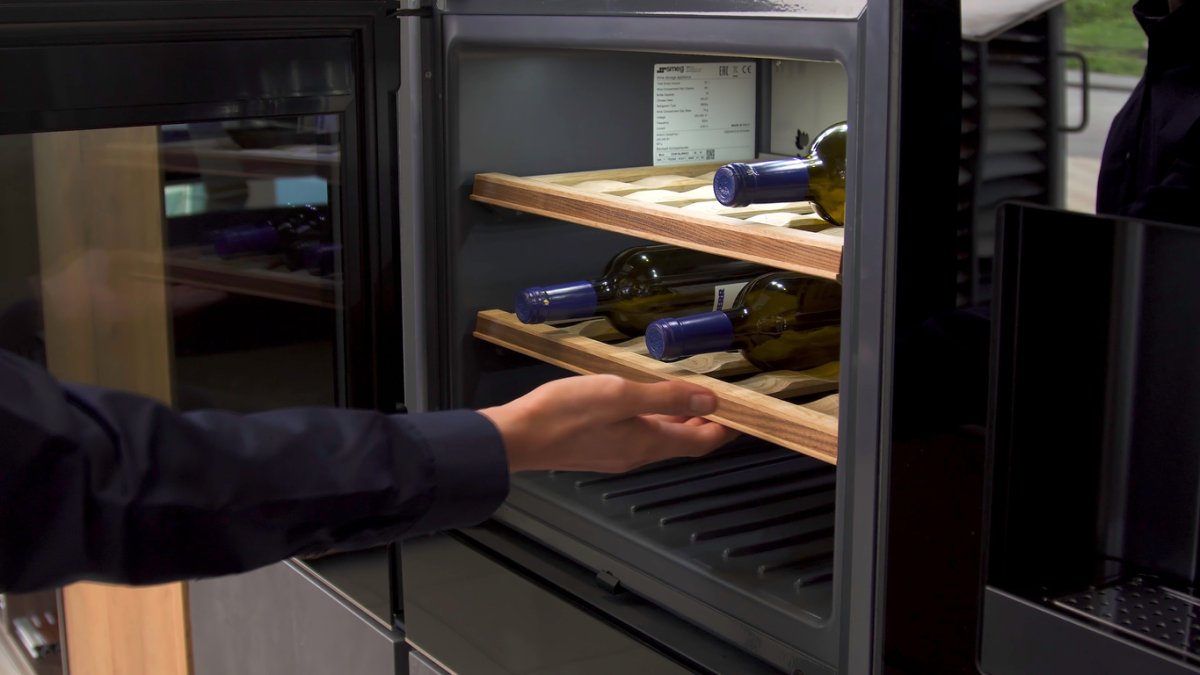 A person reaching into an open wine fridge.