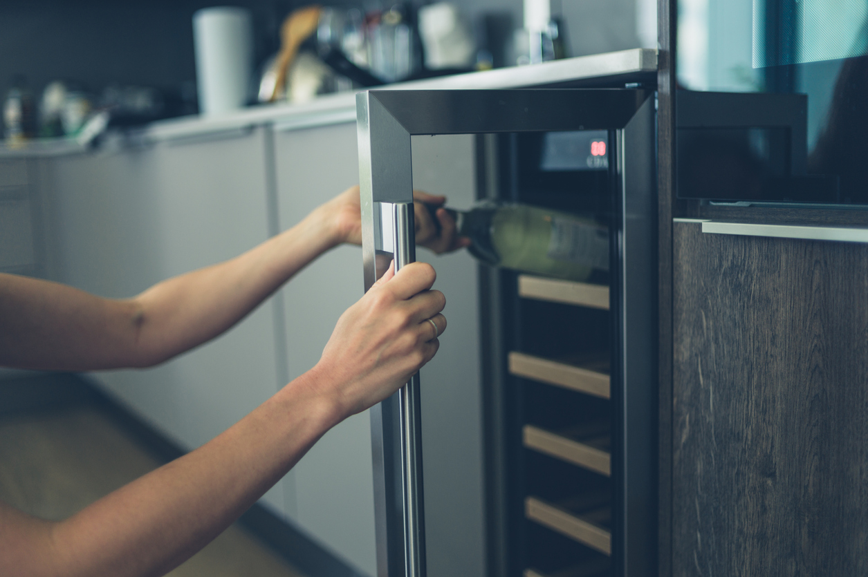 A person getting a bottle of white wine from a home wine fridge.