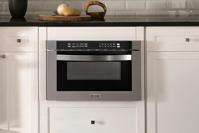 A microwave drawer installed among white cabinetry under a dark kitchen counter.