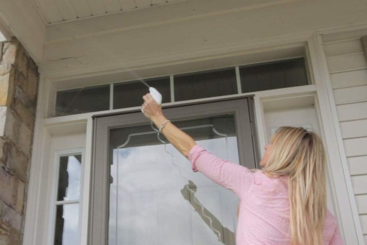 A person spraying Wet & Forget Miss Muffet's Revenge spider repellent onto a roof overhang.