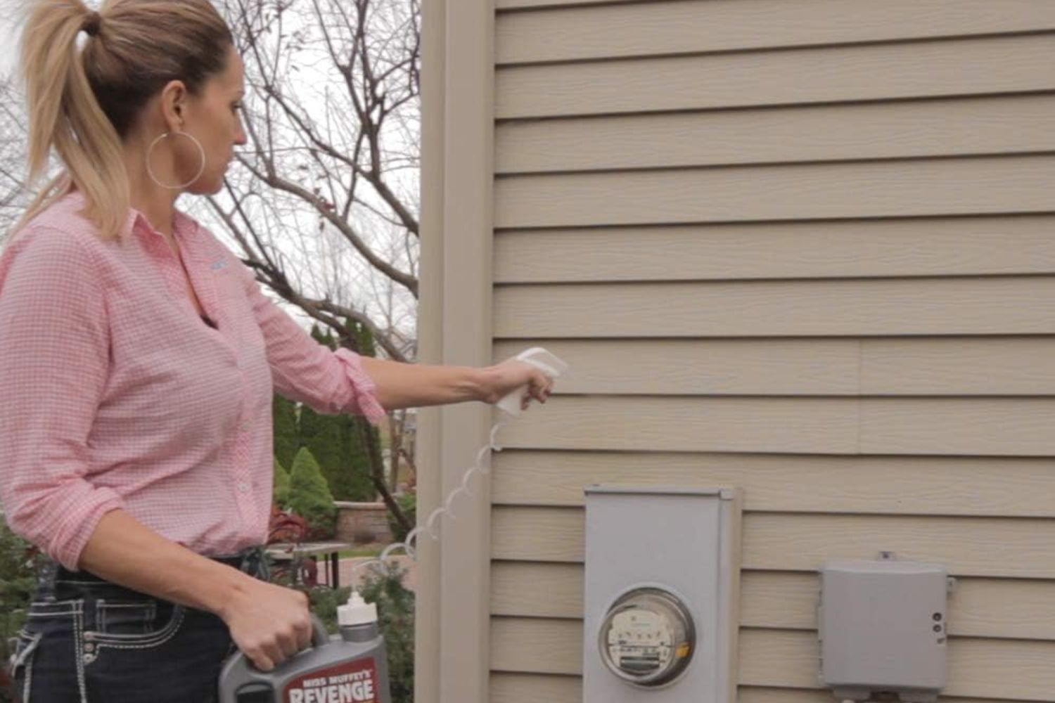 A person spraying Wet & Forget Miss Muffet's Revenge spider repellent on house siding.