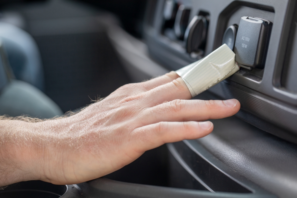 Hand with tape around fingers cleaning car buttons.