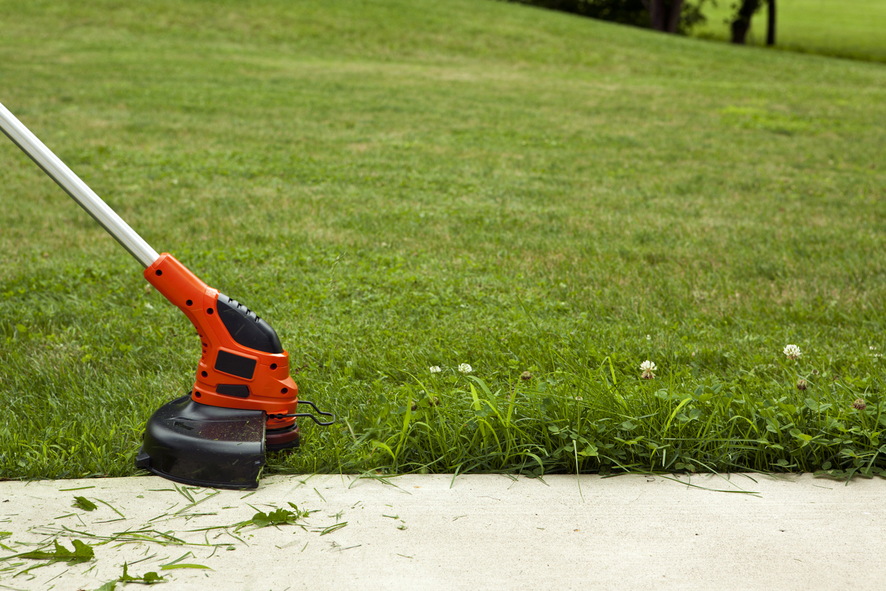 Person uses string trimmer to edge the lawn alongside a driveway.