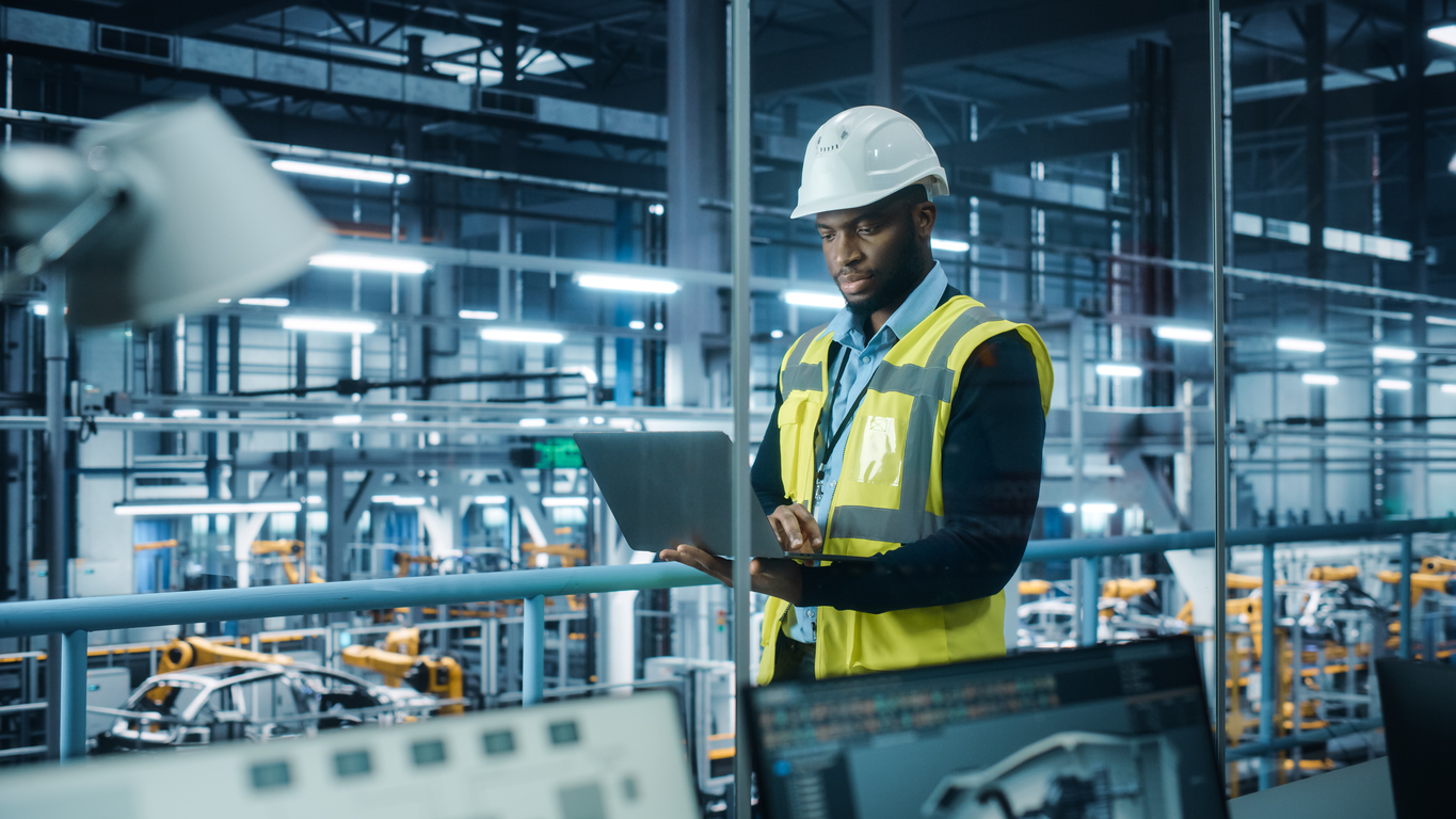 A-Black-construction-engineer-works-on-a-laptop-in-an-industrial-building.