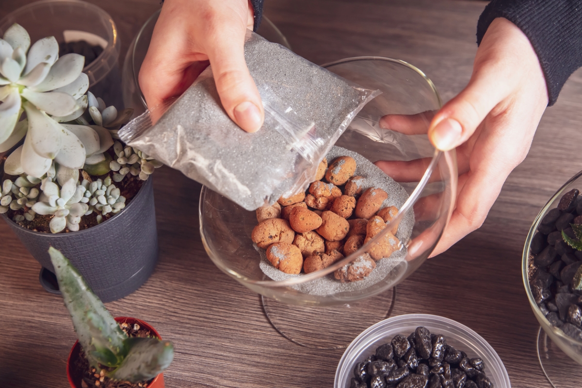 Person putting gravel and sand in glass bowl.