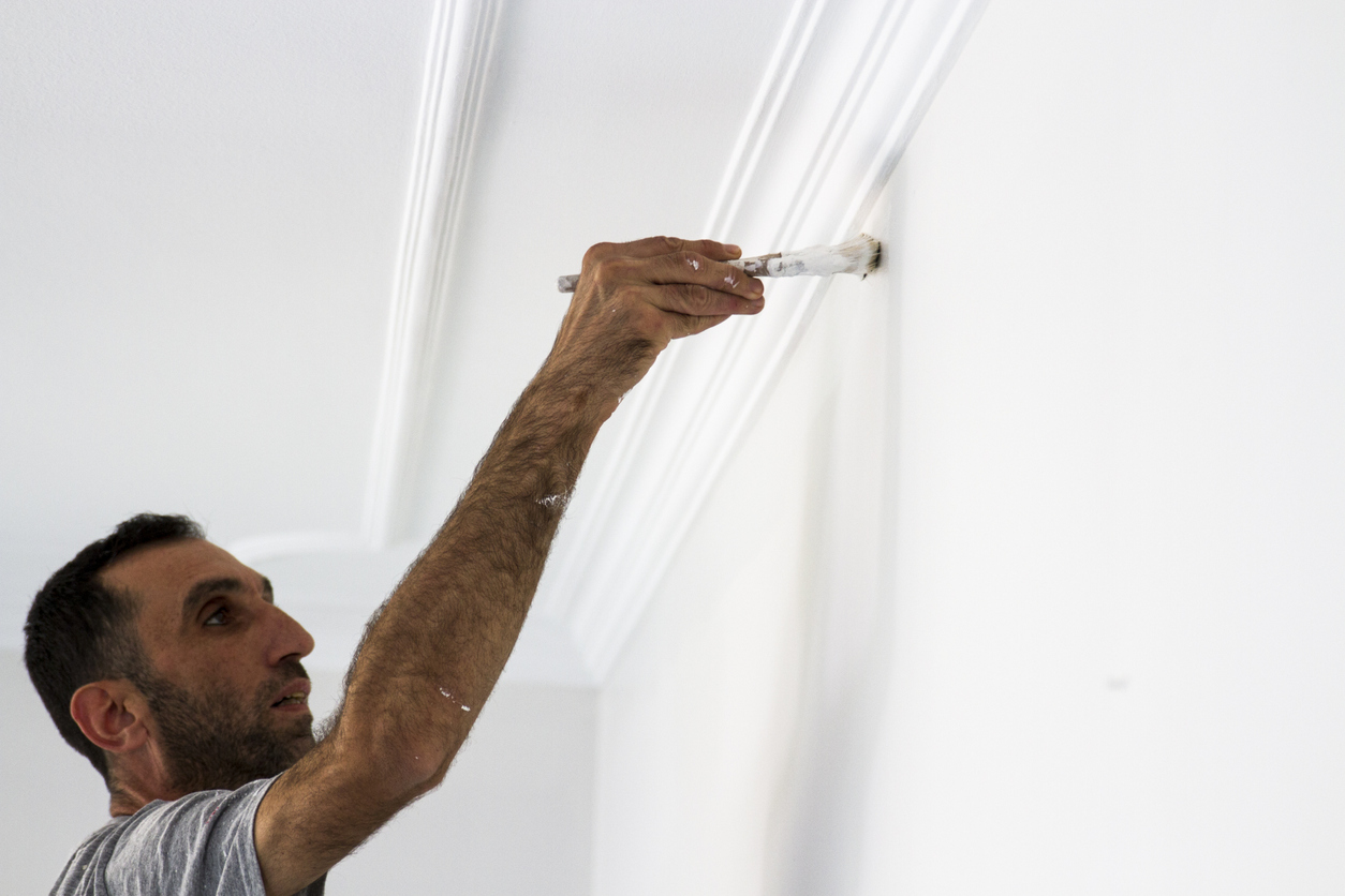 Man paints crown molding white.