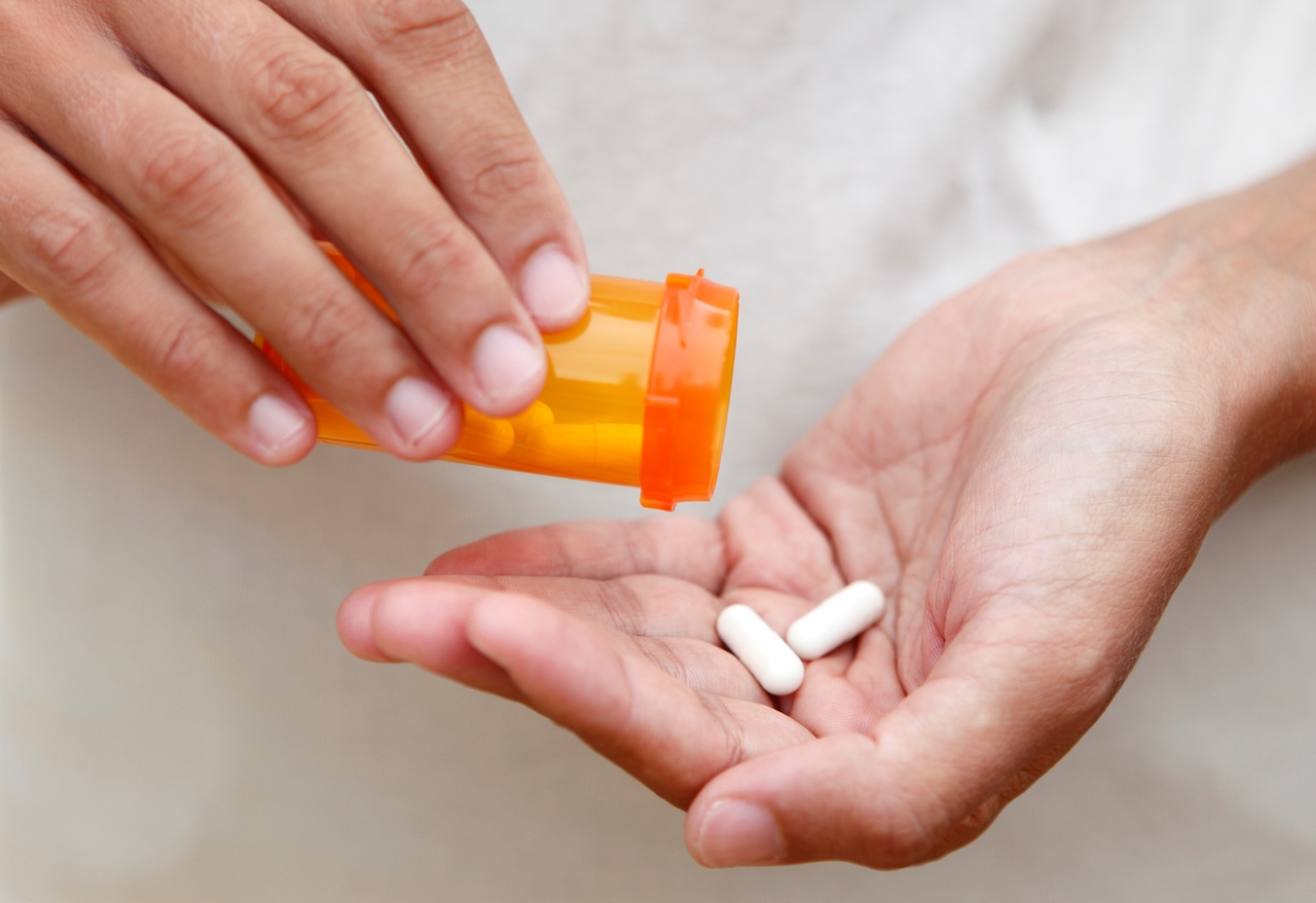 Person getting pills from pill bottle.