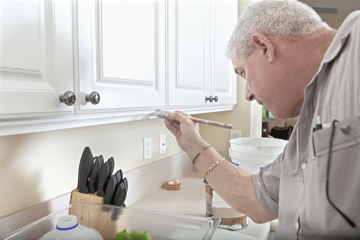 Mature man paints kitchen cabinets white.