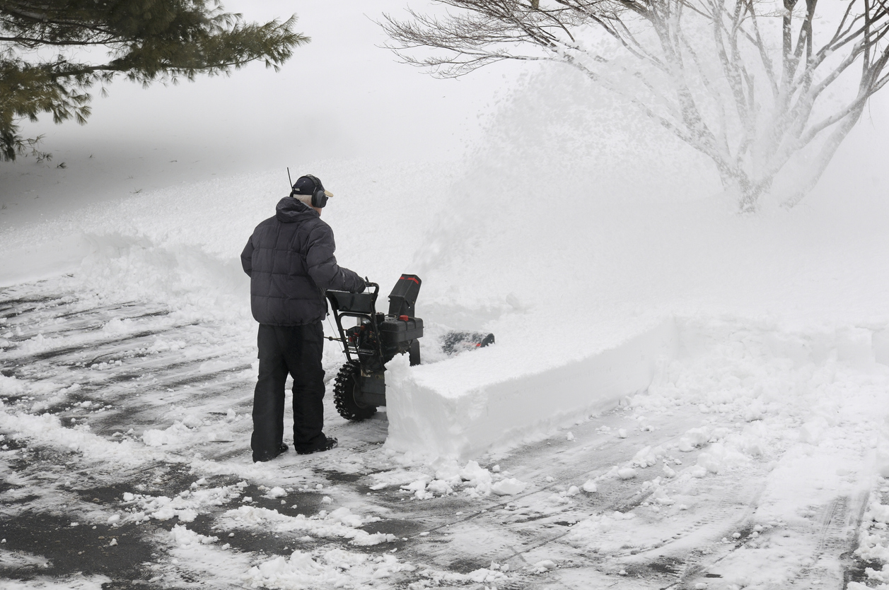 Man snow blowing rows of snow in driveway.