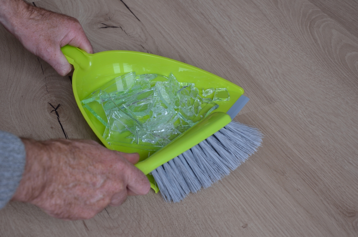 Hands sweeping broken glass into dustpan.