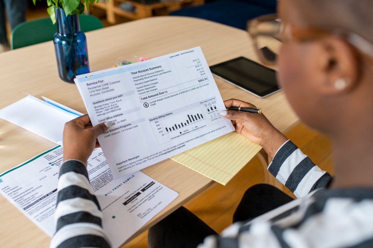 Over-the-shoulder view of a young woman in glasses looking at a utility bill.