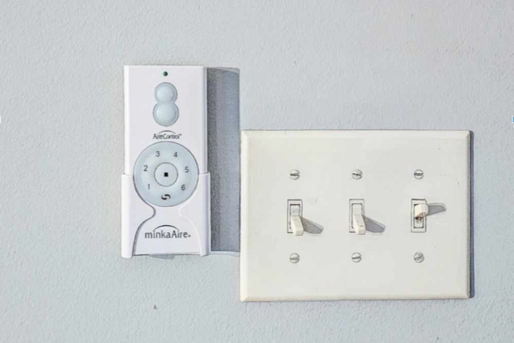 The remote for the Barn by Minka-Aire ceiling fan installed on the wall next to a light switch.