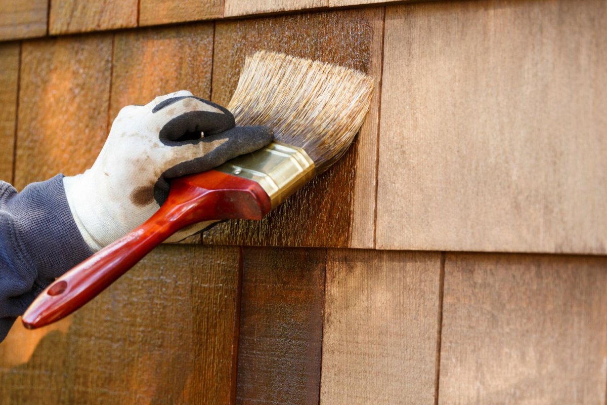 A close up of a gloved hand finishing cedar siding.