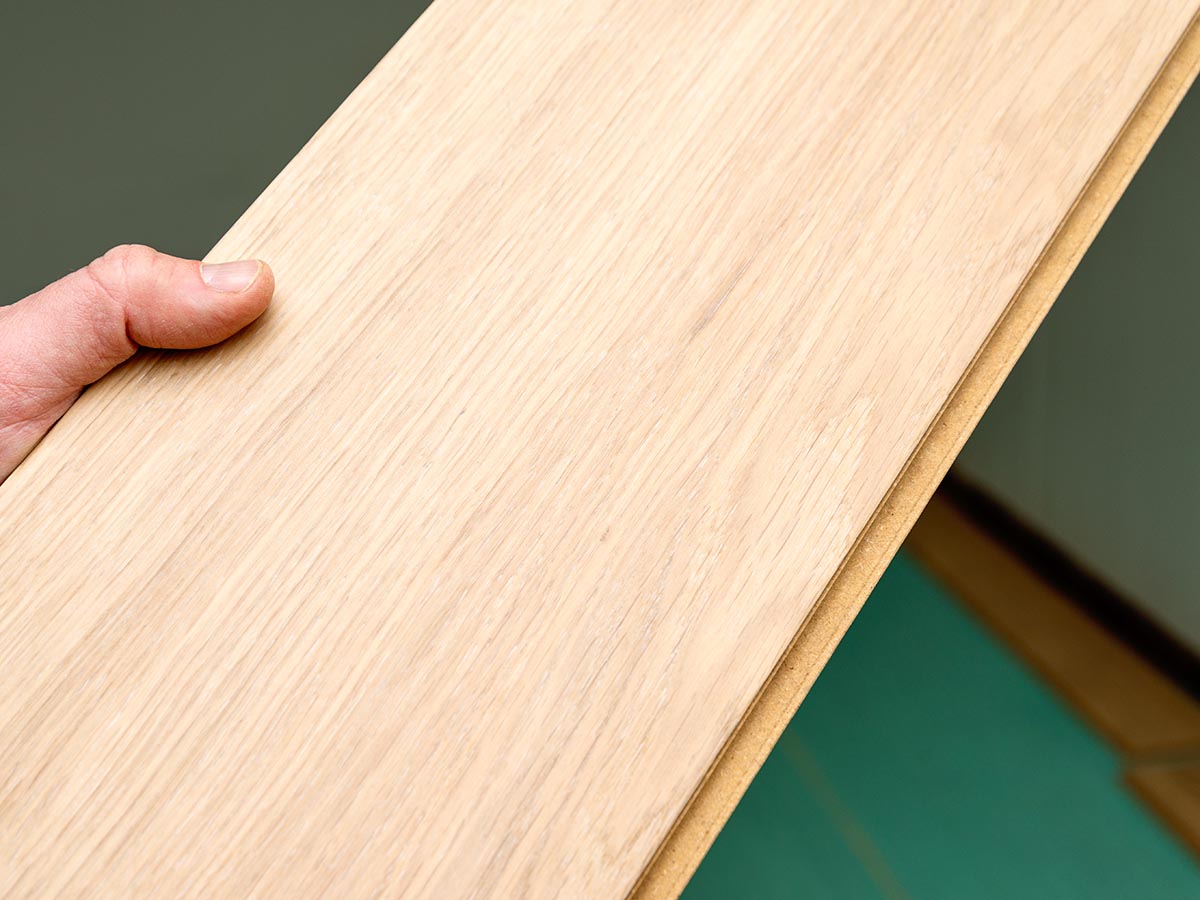 A person holding up a piece of Flooret engineered hardwood flooring during installation and testing.