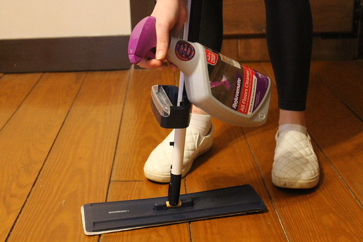 A person spraying a wood floor with Rejuvenate All Floors Cleaner before mopping.