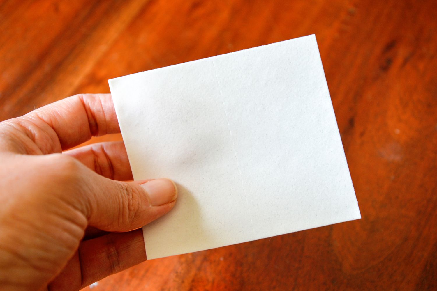 A person holding a square True Earth laundry detergent sheet before using it in testing.