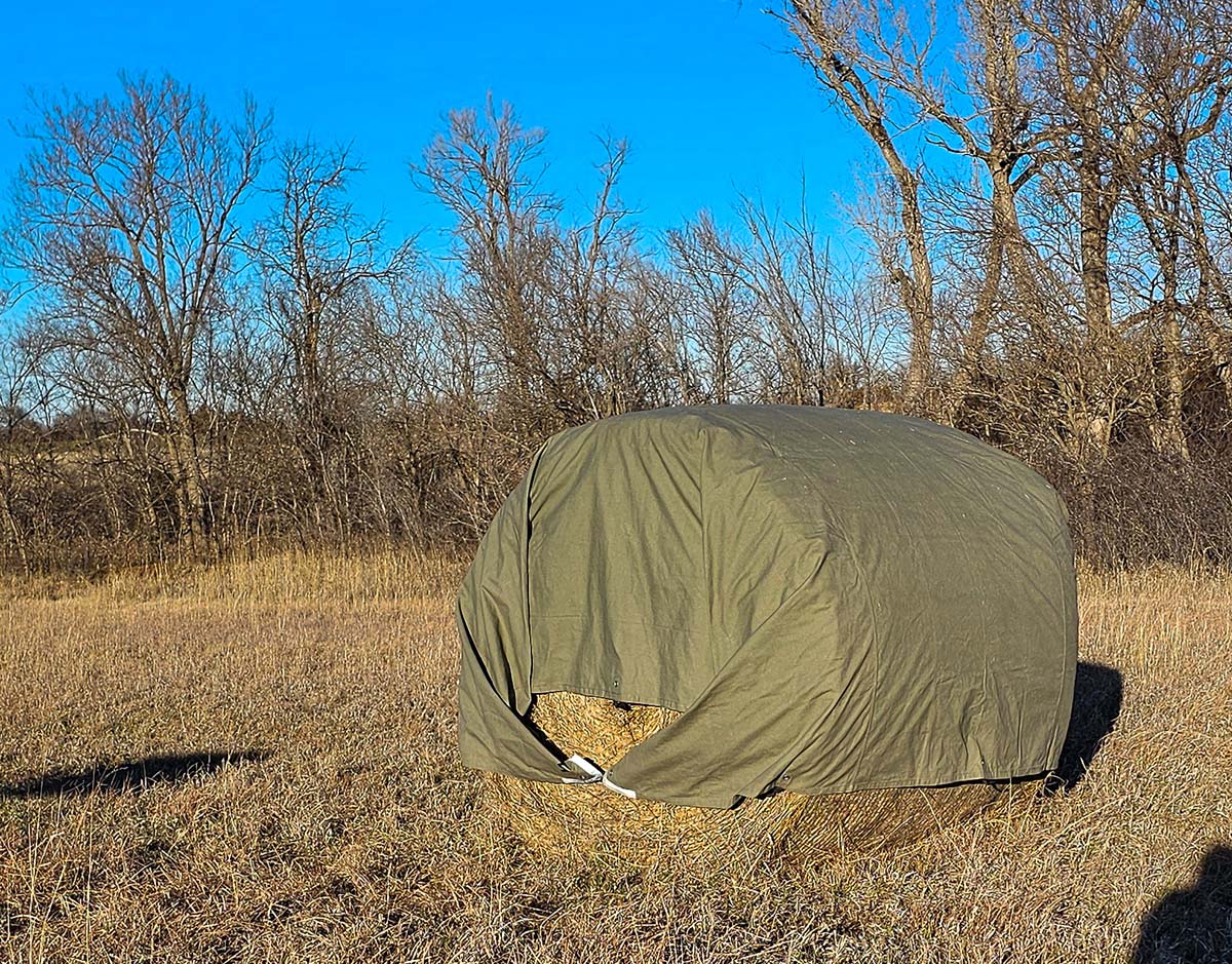 The White Duck Tarp pulled tight around a bale of hay in a field.