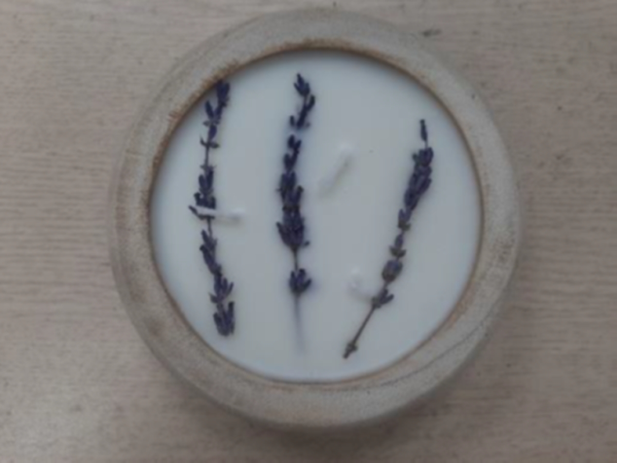 A candle with lavender stems in wooden bowl.