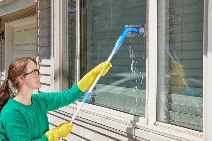 Woman uses microfiber mop to clean exterior windows of a home.