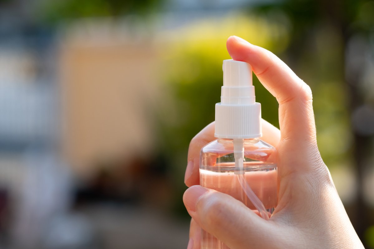 A person holding a spray bottle with a clear liquid inside.