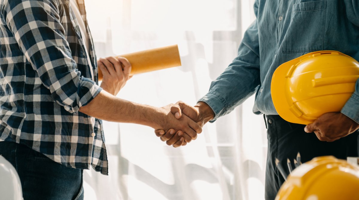 Man shakes hand of home contractor holding a yellow hardhat.