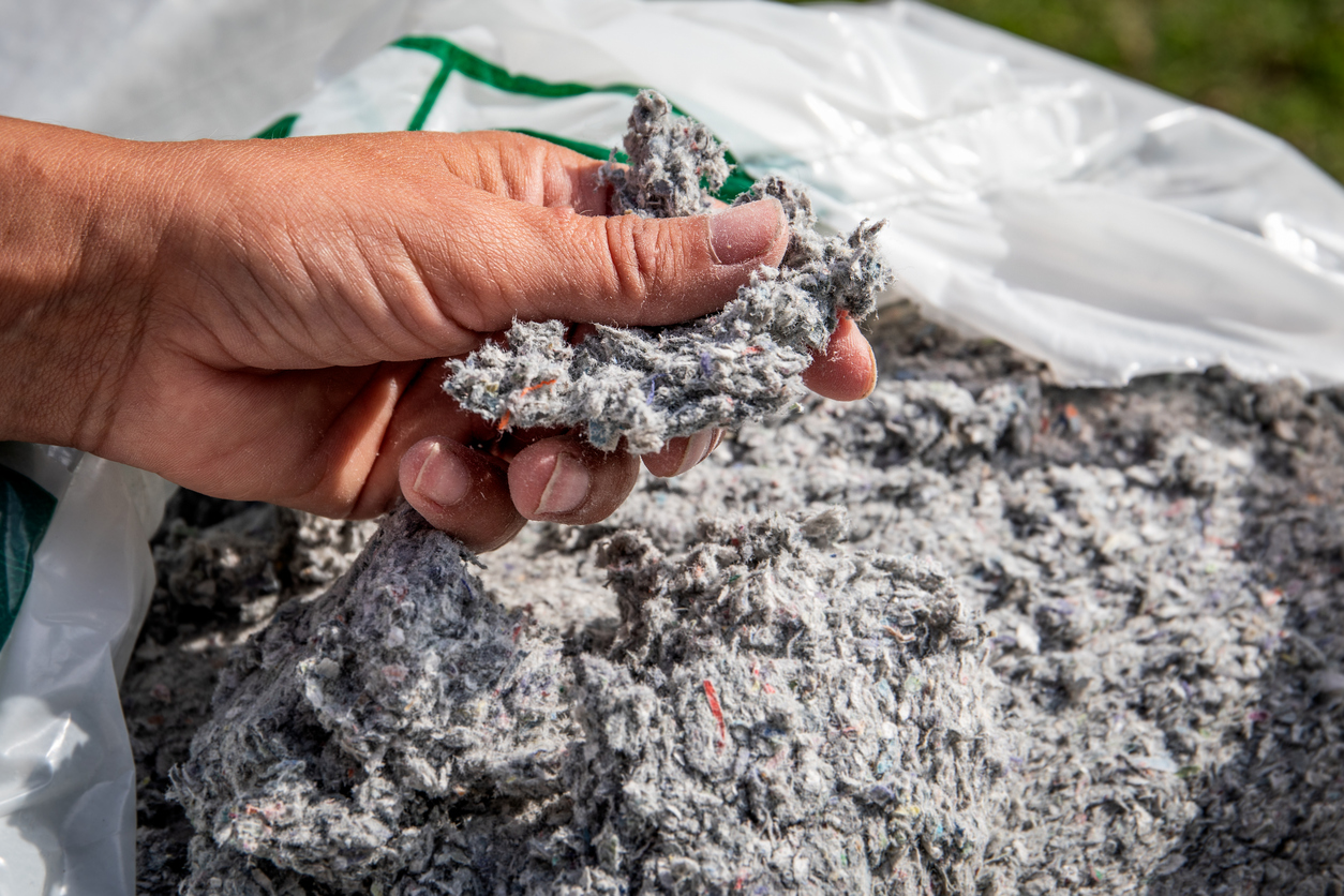 A-hand-holds-a-sample-of-blow-in-cellulose-over-a-bag-full-of-it.