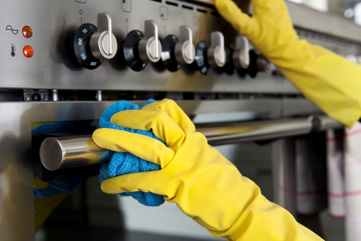 Yellow gloved hands cleaning steel stove.