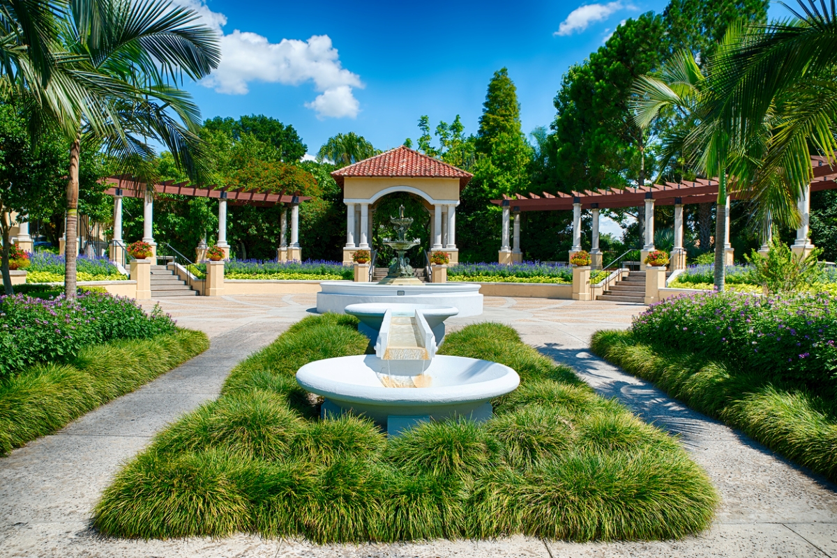 View of fountain at public park with grassy landscape and trees.