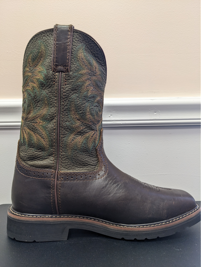 A brown work boot with detailing sits on a table against a wall.