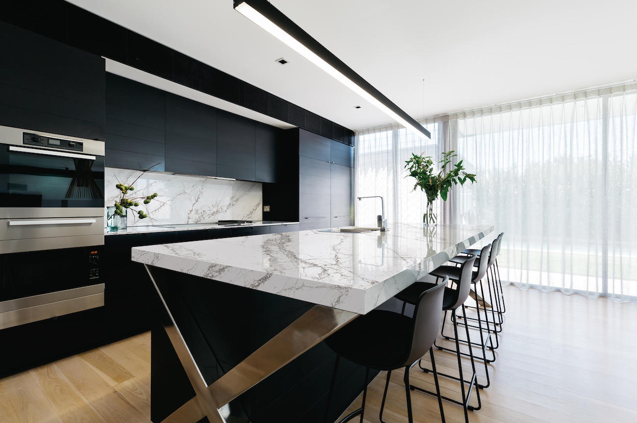 A kitchen with dark cabinets has a marble countertop and solid slab backsplash.