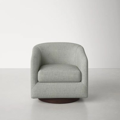 The AllModern Bennett Upholstered Swivel Barrel Chair on a grey floor in an empty room.