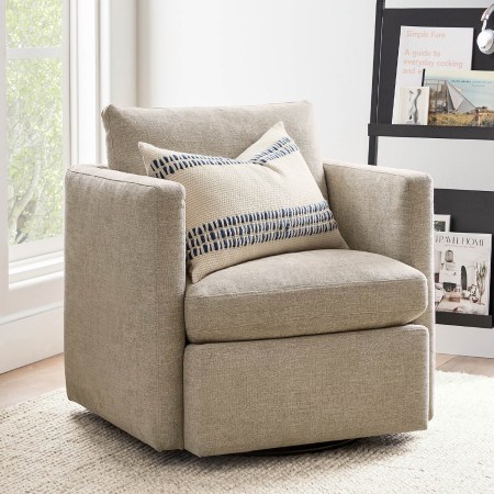  The Pottery Barn Menlo Upholstered Swivel Armchair on a rug next to a window and bookshelf.