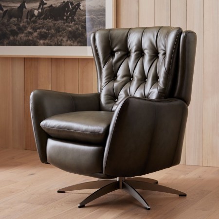  The Pottery Barn Wells Tufted Leather Swivel Recliner on a wood floor in a wood-paneled rule.